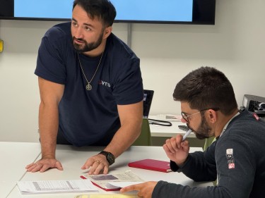 Two men, one a learner and one an instructor in a training room at a table.