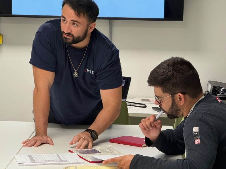 Two men, one a learner and one an instructor in a training room at a table.