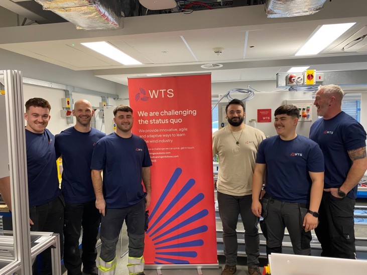 5 learners in WTS t-shirts standing aorund a red banner with a man in a sand t-shirt